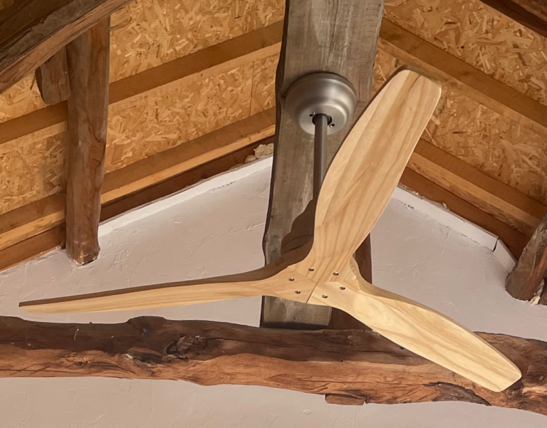 Professional assembly and fixture of a modern timber ceiling fan on a structural beam in a barn renovation.